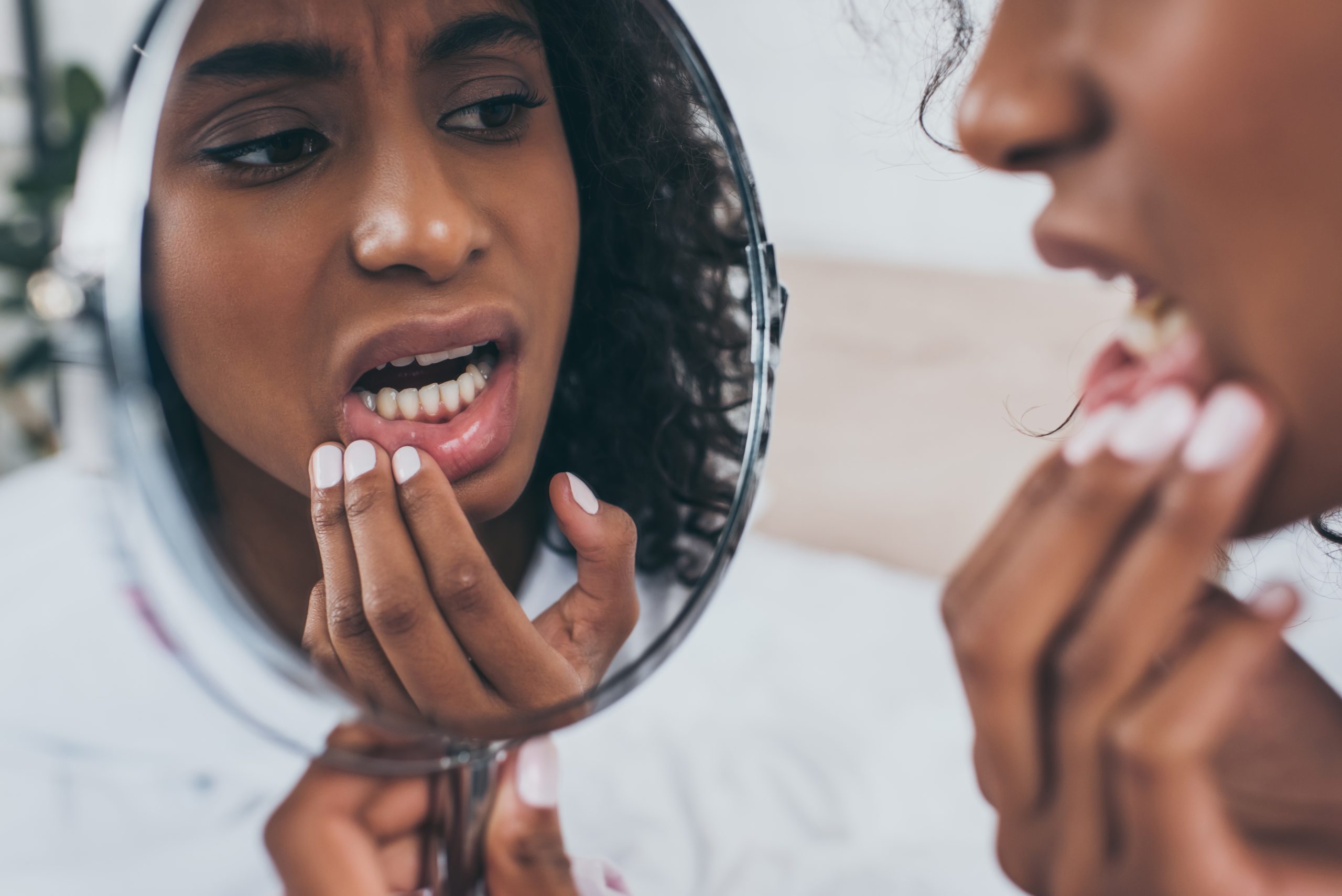 Young woman with painful gums looking in a handheld mirror